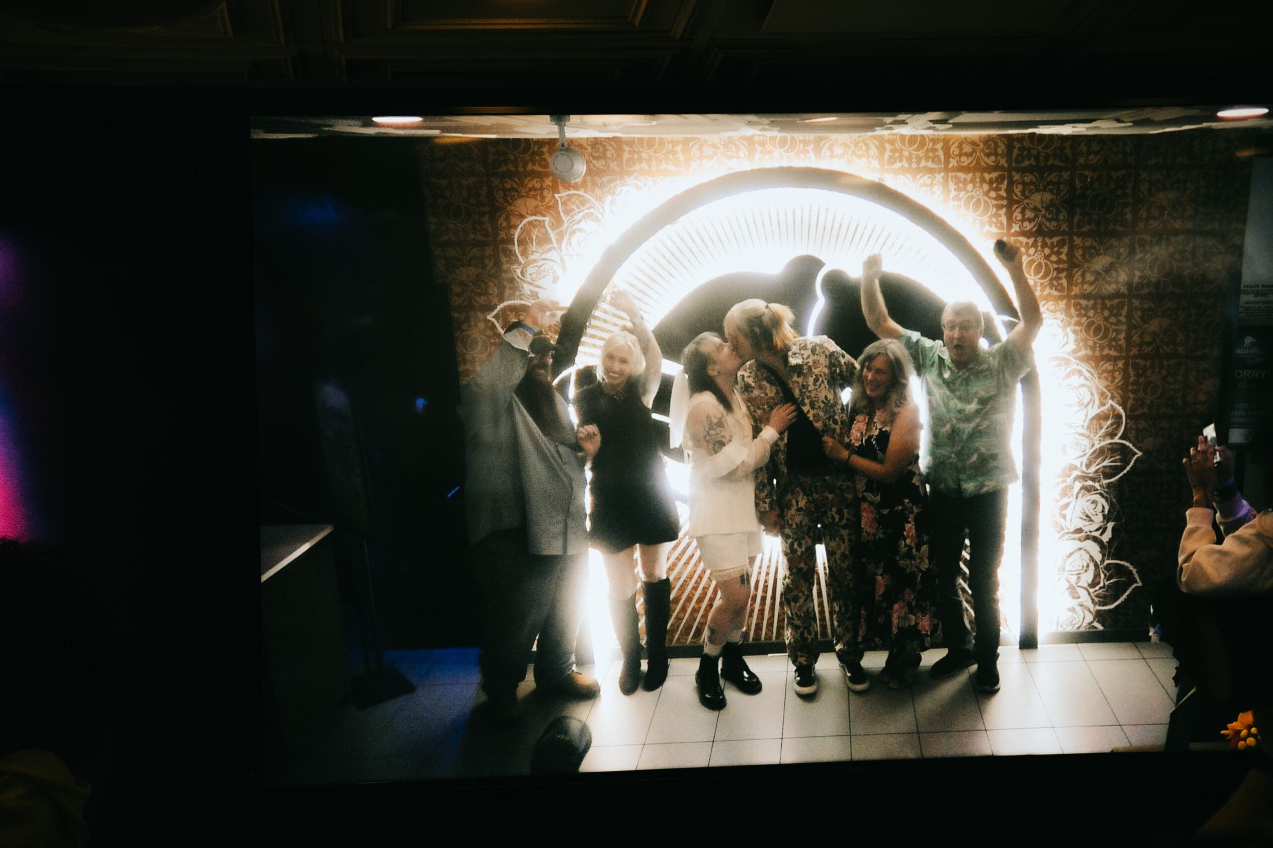 bride and groom share a kiss as their wedding party celebrate around them