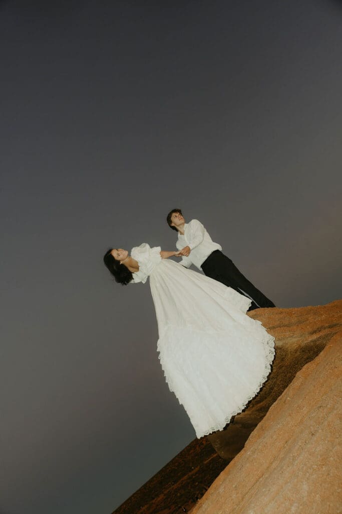 bride and groom hold hands and lean off a red rock