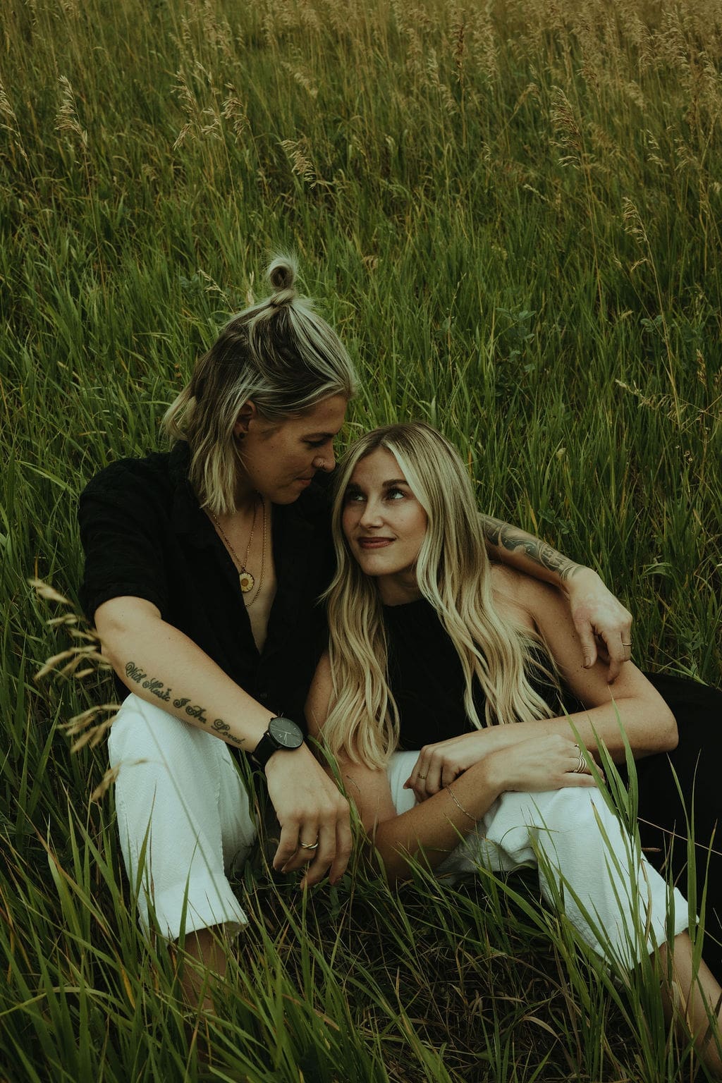 couple sit in a tall grass field together during their flatiron engagement photos