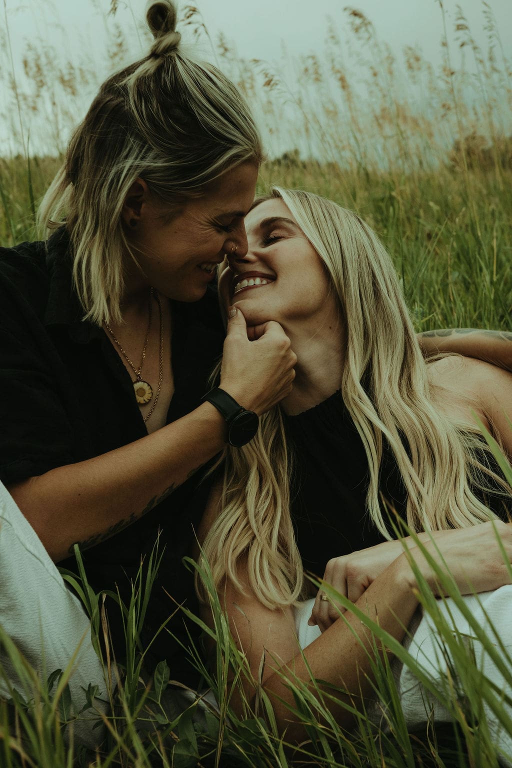 couple sit in a tall grass field together during their flatiron engagement photos as they share intimate moments together