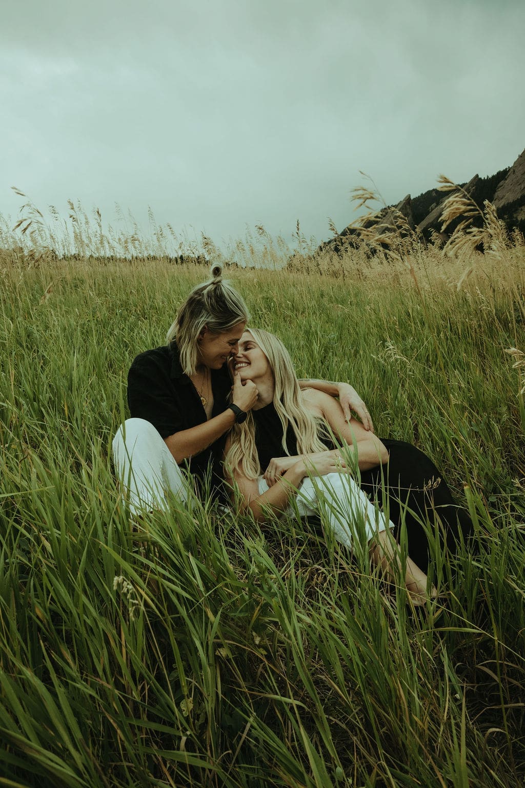 couple sit in a tall grass field together during their flatiron engagement photos as they share intimate moments together