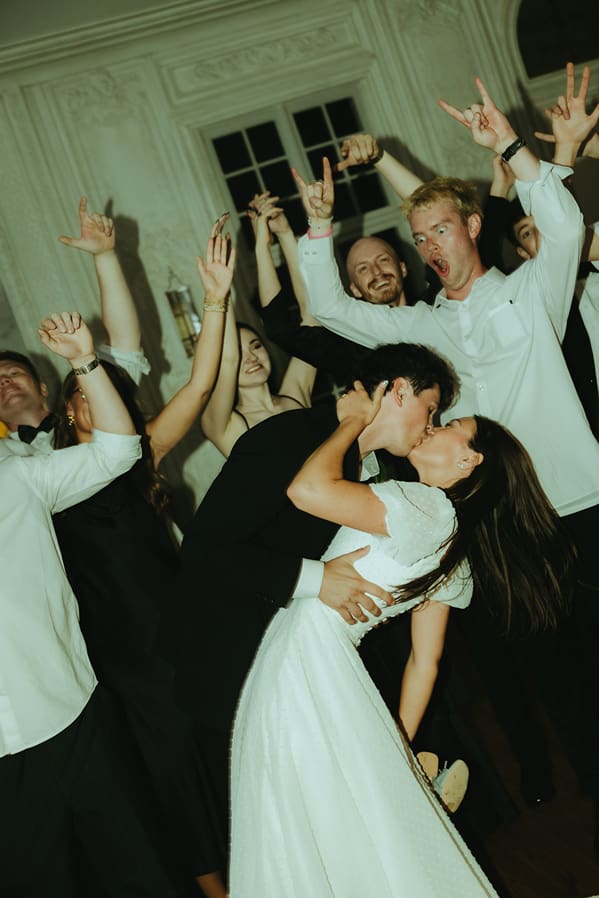 bride and groom share a kiss as their guests celebrate in the background captured by southern Utah photographer Kennedi Brooke photo